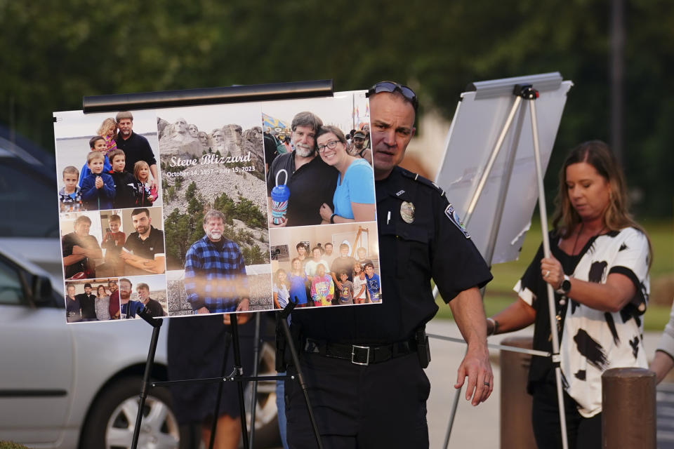 A Hampton police officer carries photos of Steve Blizzard, one of the victims of Saturday's mass shooting, to a vigil, Monday, July 17, 2023, in Hampton, Ga. (AP Photo/John Bazemore)