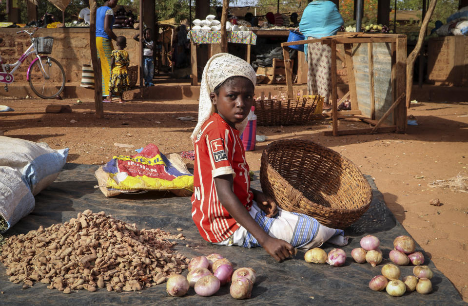 In this Wednesday, May 13, 2020, photo, a child sits on the ground selling onions at a market stall in Tougan, Burkina Faso. Violence linked to Islamic extremists has spread to Burkina Faso's breadbasket region, pushing thousands of people toward hunger and threatening to cut off food aid for millions more. (AP Photo/Sam Mednick)