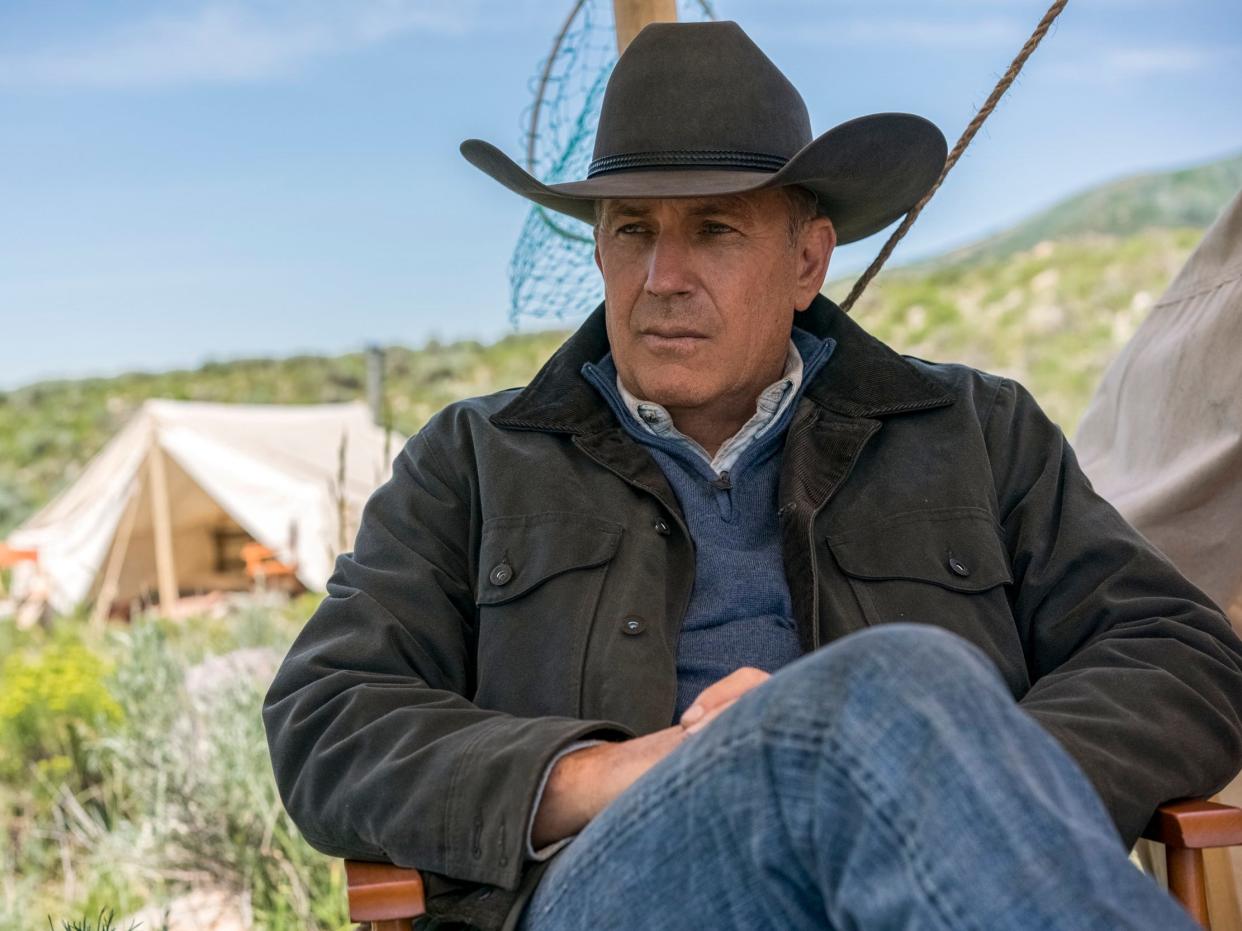 A scene of Kevin Costner in "Yellowstone" where John Dutton is sitting in a chair next to a white canvas tent in an open field.