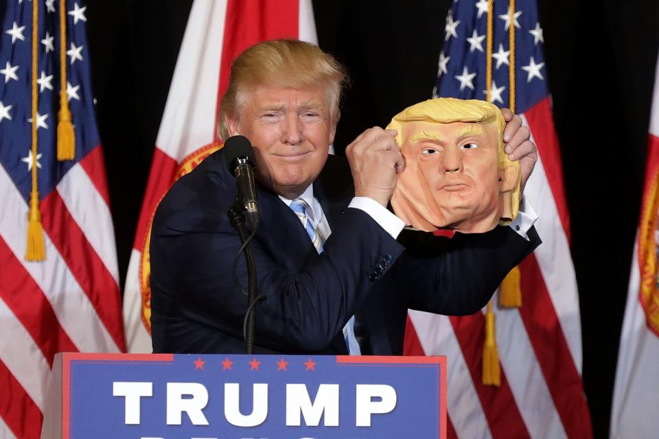 Donald Trump holds a rubber mask of himself.