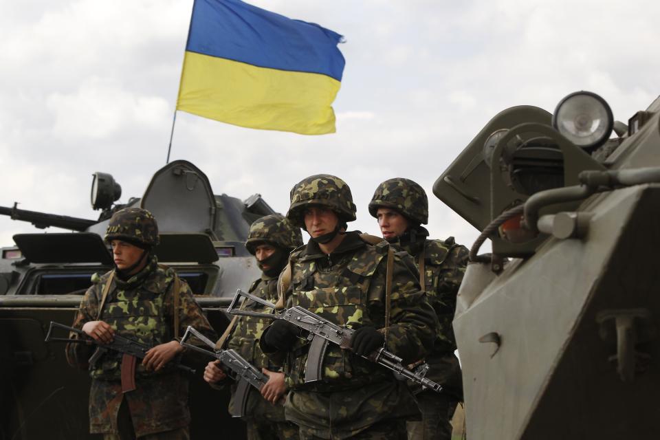 Ukrainian soldiers stand near APCs, that fly a Ukrainian flag, as the Ukrainian army troops receive ammunition in a field on the outskirts of Izyum, Eastern Ukraine, Tuesday, April 15, 2014. An Associated Press reporter saw at least 14 armored personnel carriers with Ukrainian flags, one helicopter and military trucks parked 40 kilometers (24 miles) north of the city of Slovyansk on Tuesday. (AP Photo/Sergei Grits)