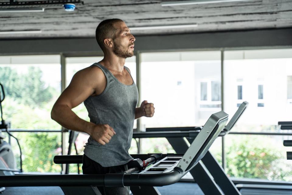 young handsome man doing cardio exercises with treadmill in gym with dumbbell fitness health club