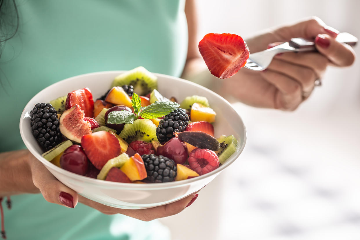 A woman breakfasts a fruit salad high in vitamins and fiber.