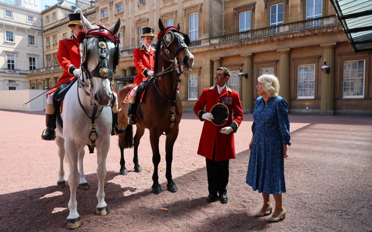 The Queen stands next to two horse riders in the quandrangle