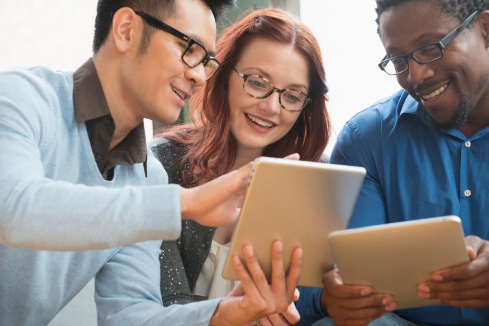 Three investors compare content on a pair of tablets. 