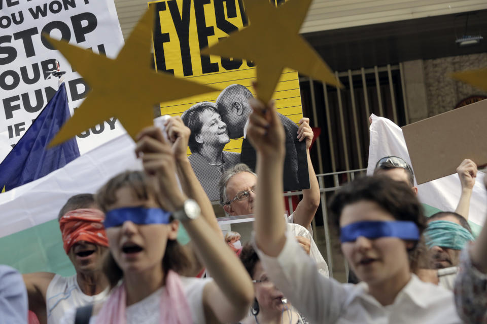 Protesters keep their eyes closed and shout in front of a poster showing German Chancellor Angela Merkel and Bulgarian Prime Minister Boyko Borissov in front of the German Embassy in Sofia, Bulgaria, Wednesday, Aug. 12, 2020. Several hundred anti-government protesters gathered on Wednesday in front of Germany’s embassy in Sofia, calling on Berlin and Brussels to “open their eyes” to widespread corruption in Bulgaria. During the peaceful protest, dubbed “Eyes Wide Shut,” organizers complained that the European Union has willfully ignored the state of affairs in its poorest member state. (AP Photo/Valentina Petrova)