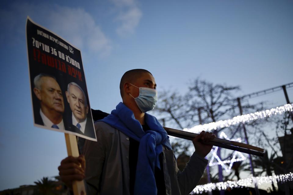 A man, wearing a mask for protection against the spread of the coronavirus, holds a poster of Israeli Prime Minister Benjamin Netanyahu, right, and Benny Gantz, left, that reads: 'a government with 36 ministers? Where is the shame?' during a protest against the government and the corruption, at Rabin square in Tel Aviv, Israel, Saturday, May 2, 2020. Several thousand Israelis took to the streets on Saturday night, demonstrating against Prime Minister Benjamin Netanyahu's new coalition deal with his chief rival a day before the country's Supreme Court is to begin debating a series of legal challenges to the agreement.(AP Photo/Ariel Schalit)