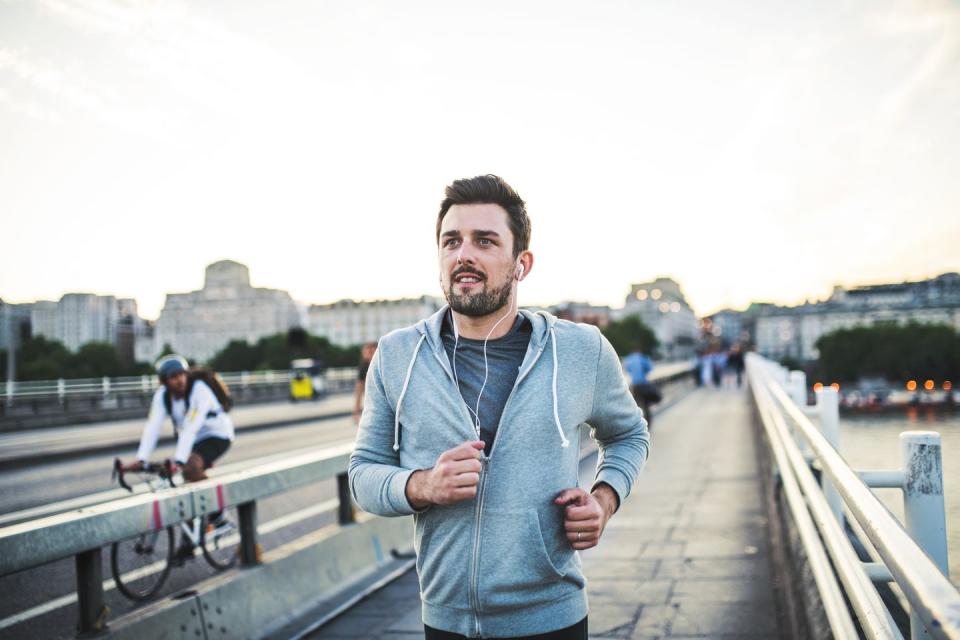 Young sporty man with earphones running on the bridge outside in a city.