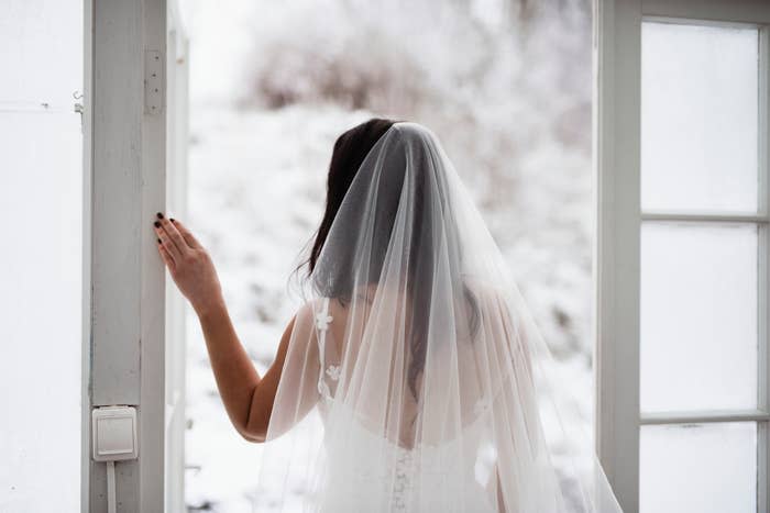 Bride in a white dress and veil looks out a window with a snowy landscape outside