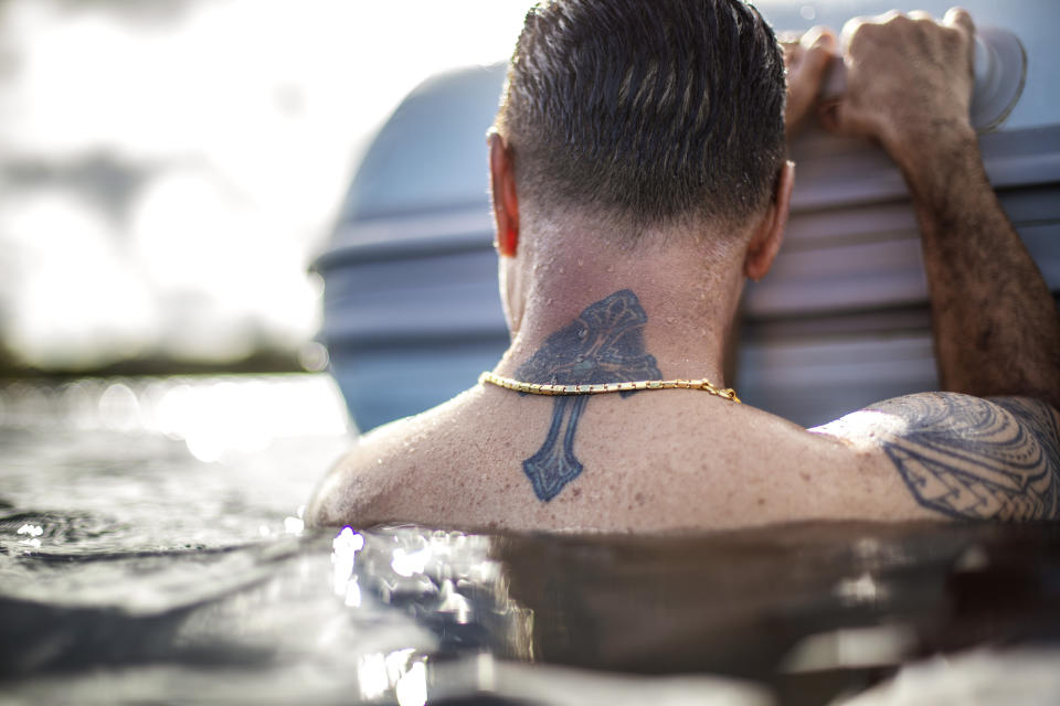A tattoo of a cross decorates the neck of Walter Denton as he rests on the side of a boat while swimming in the ocean with his brother in Agat, Guam, Saturday, May 11, 2019. Denton, one of over 200 former altar boys, students and Boy Scouts who are now suing Guam's Catholic archdiocese for sexual abuse, still thinks about what happened almost every day. After decades away from the church, the former altar boy is once again attending Mass. "People ask me, 'Walter, how are you doing?' And I say I'm blessed. God has blessed me." (AP Photo/David Goldman)