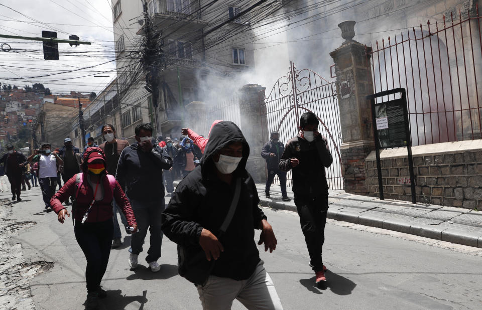 La gente huye de los gases lacrimógenos mientras la policía dispersa a los manifestantes que protestan en apoyo de los trabajadores de la salud en medio de la pandemia de COVID-19 en La Paz, Bolivia, el lunes 22 de febrero de 2021. Los trabajadores de la salud han convocado una huelga general para protestar contra una nueva ley sanitaria de emergencia que, entre otras cosas, permite la contratación de médicos extranjeros. (AP Foto/Juan Karita)