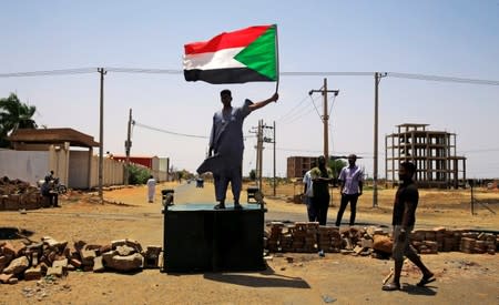 A Sudanese protester holds a national flag as he stands on a barricade along a street, demanding that the country's Transitional Military Council hand over power to civilians, in Khartoum