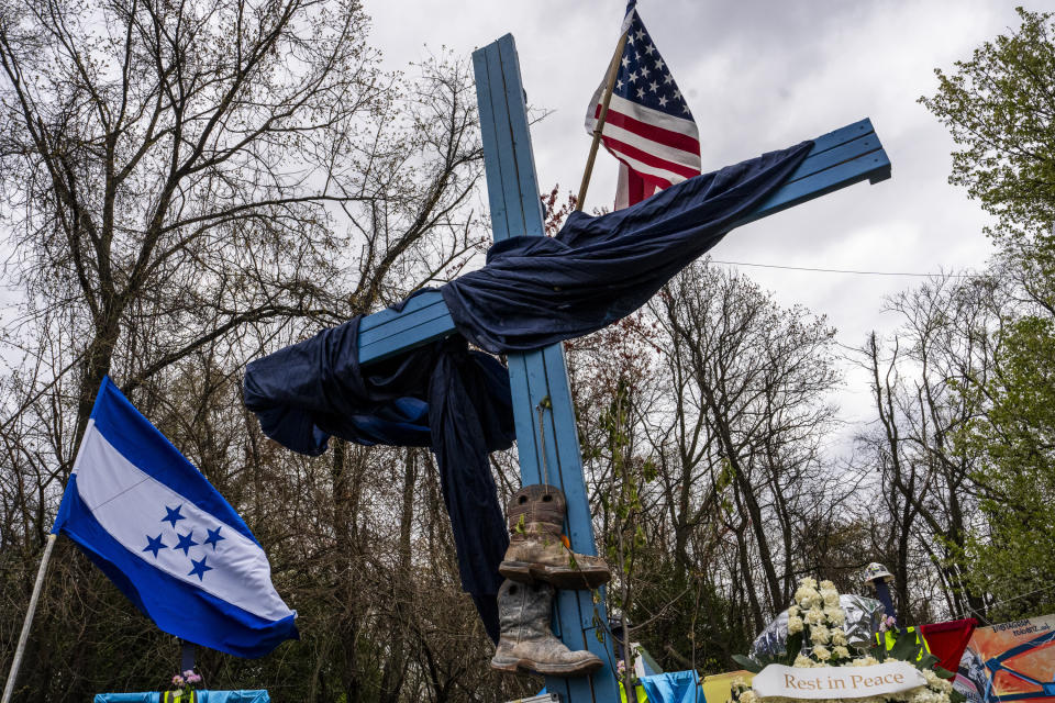 A memorial site to honor the construction workers who lost their lives in the collapse of the Francis Scott Key Bridge sits on the side of the road near the blockade to Fort Armistead Park, in Baltimore, Saturday, April 6, 2024. Roberto Marquez, an artist from Dallas, painted a mural in their honor as well as painted their names on several crosses dotting the perimeter of flowers, candles and other items of remembrance. Members of the community honored the victims through prayer and song. (Kaitlin Newman/The Baltimore Banner via AP)