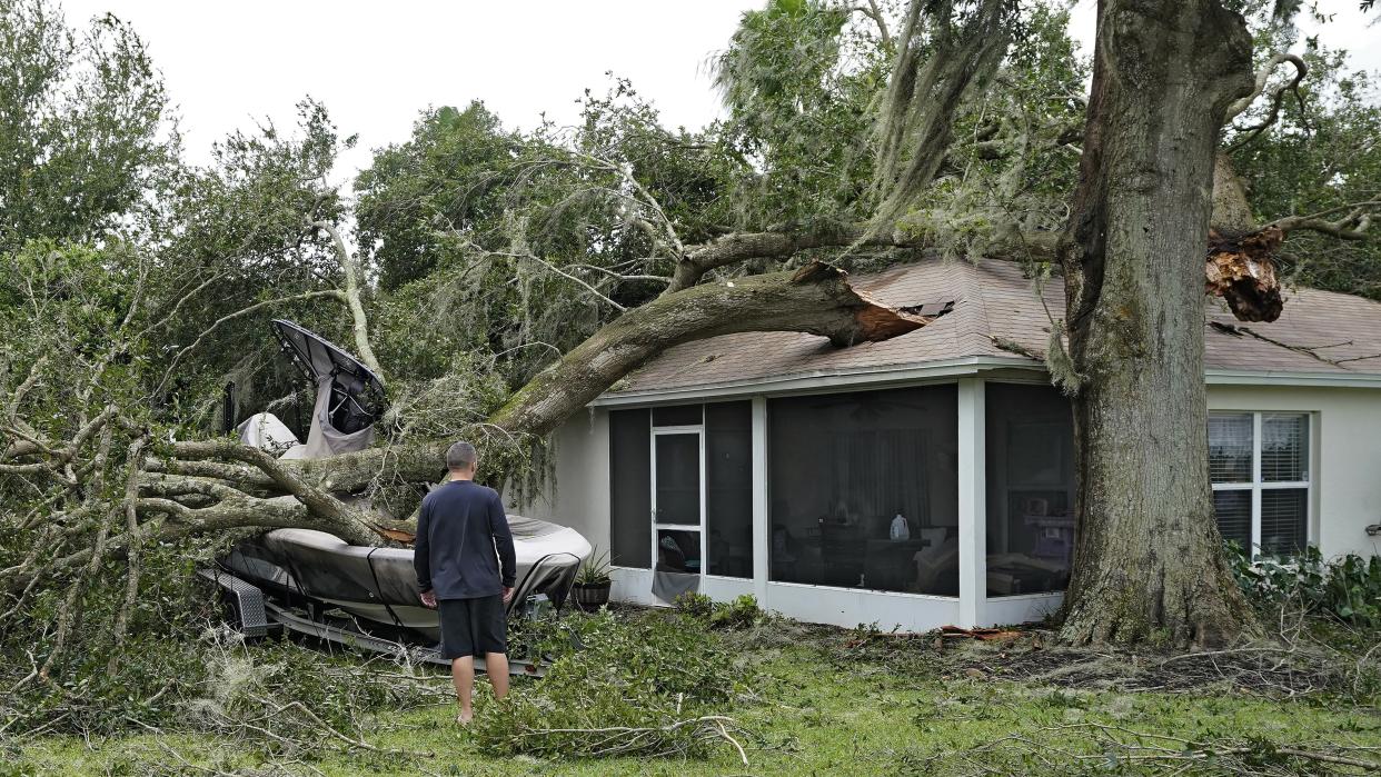 A man stands in the yard outside his home in Valrico, Fla., looking at a tree that has fallen on to his roof, creating a large hole in the structure.