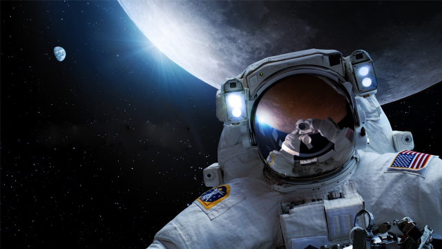  artist's impression of an astronaut with the moon behind. the astronaut is spacesuited and the reflection of their helmet shows the gloved hands holding a camera, reflected in the helmet visor. far behind is the sun peeking behind the moon, and a half-full earth. 