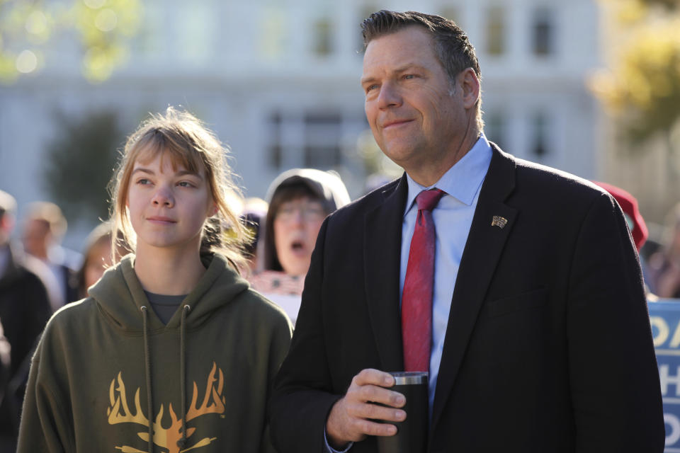 Former Kansas Secretary of State Kris Kobach, right, follows a rally against COVID-19 vaccine mandates with his oldest daughter, 15-year-old Reagan, left, outside the Kansas Statehouse, Saturday, Oct. 30, 2021, in Topeka, Kan. Kobach is a strong opponent of vaccine mandates and is running for Kansas attorney general after having lost races for governor in 2018 and the U.S. Senate in 2020. (AP Photo/John Hanna)