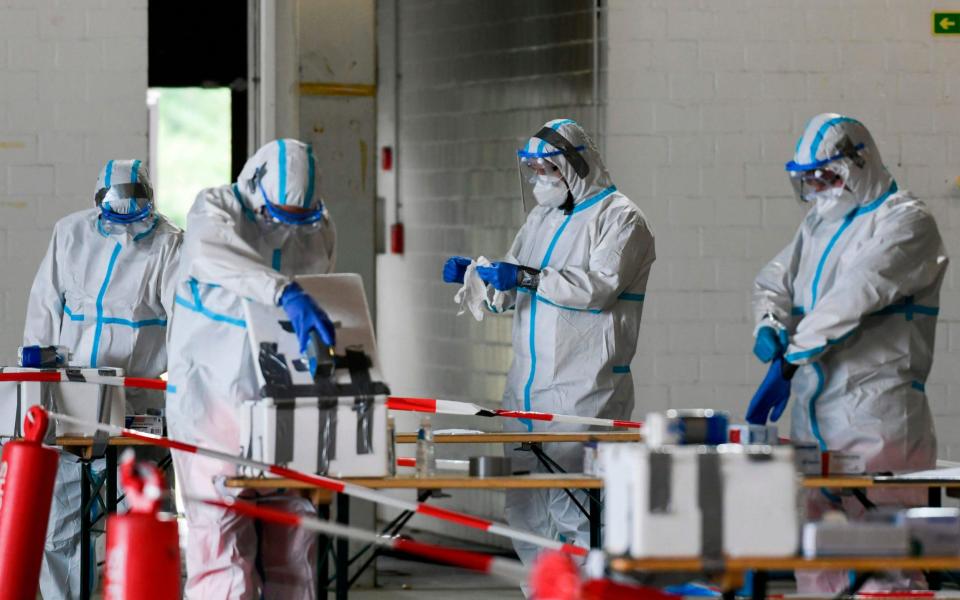 Helpers in protective suits prepare to take samples to test people in their vehicle at a coronavirus testing station set up at the former Guetersloh military airport -  INA FASSBENDER/AFP