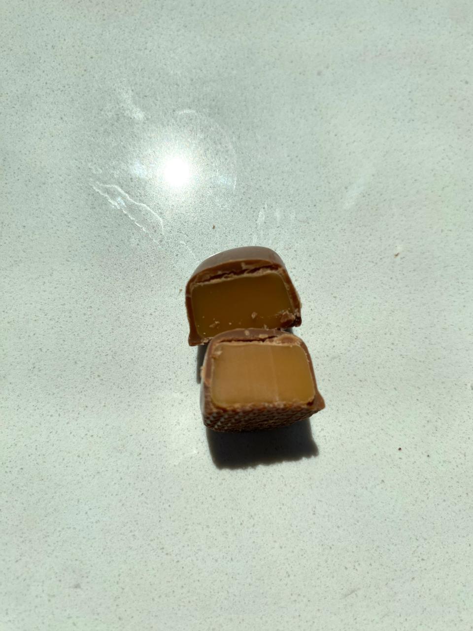 A cross-section of a filled chocolate, showing its caramel center against a light background