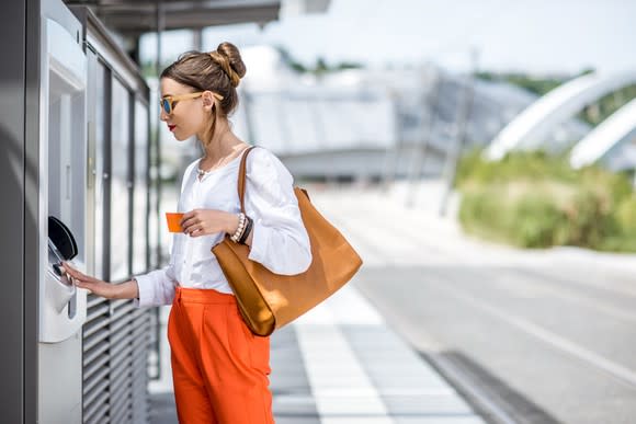 Young woman using ATM machine outdoors at a public transit station.