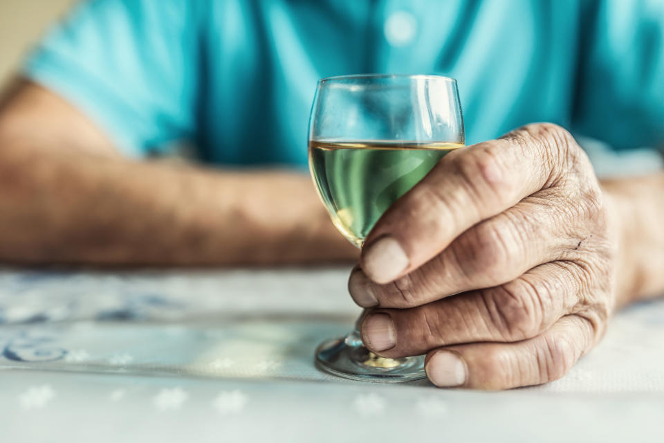 Close-up of an older person's hand holding a glass of white wine