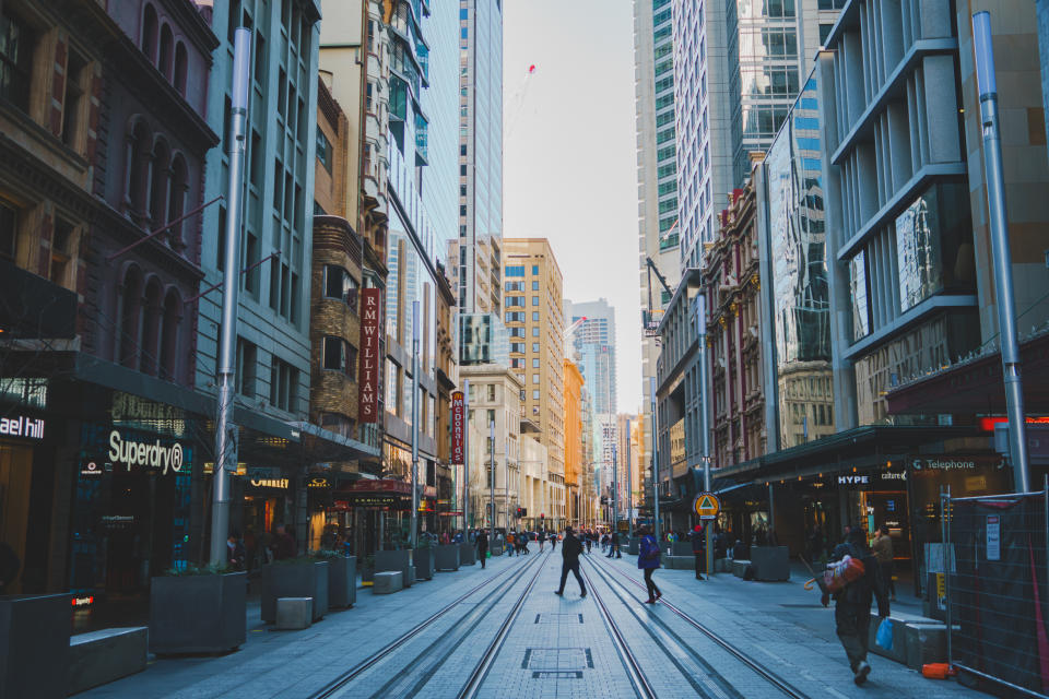 Street scene on a quiet weekend morning in central Sydney. The under construction tram lines, shopfronts, skyscrapers and pedestrians are visible in the image.