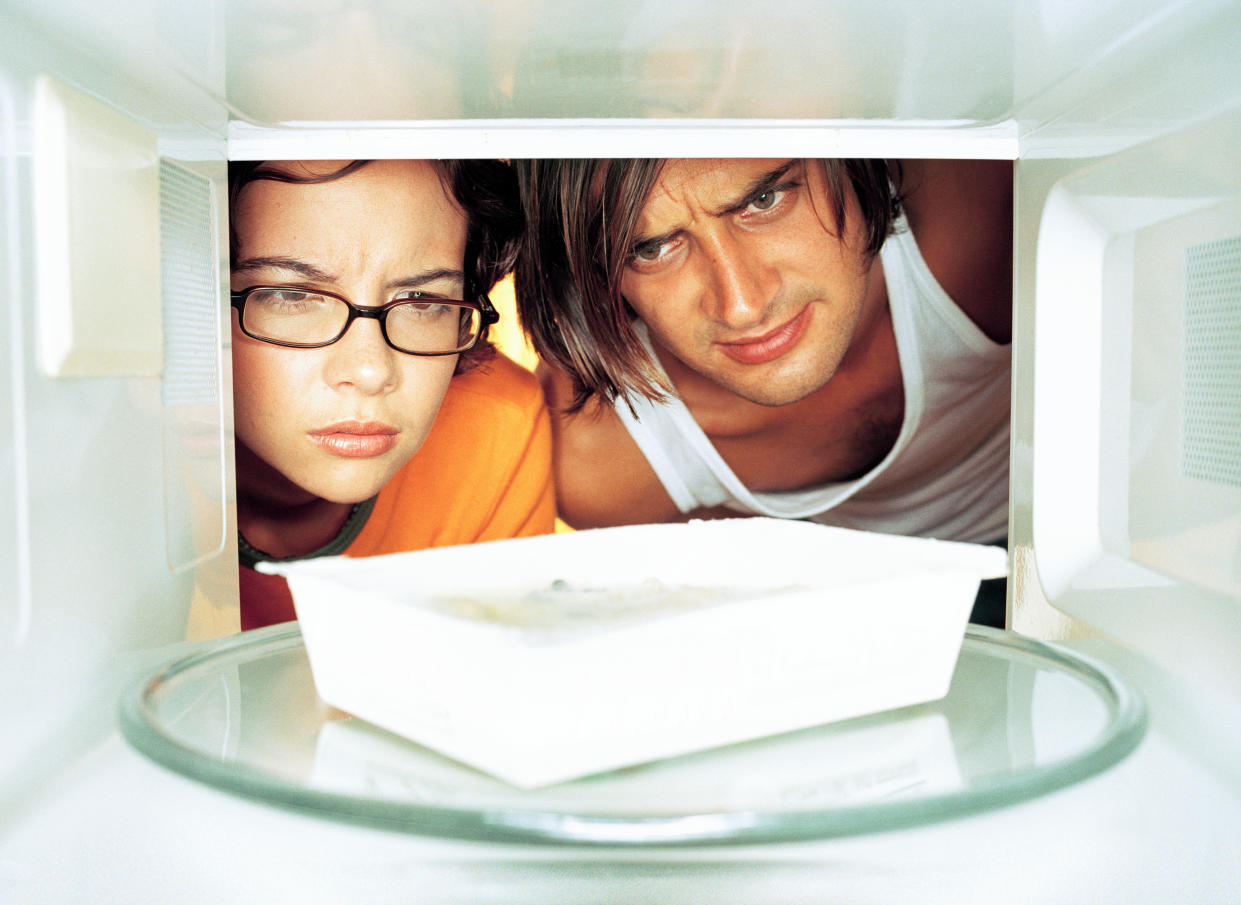 A man and woman peer into a microwave oven. 