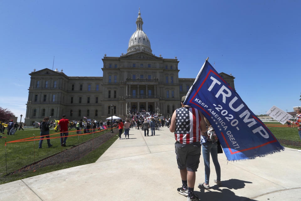 Protesters carry a Trump 2020 flag at the State Capitol during a rally in Lansing, Mich., Wednesday, May 20, 2020. Barbers and hair stylists are protesting the state's stay-at-home orders, a defiant demonstration that reflects how salons have become a symbol for small businesses that are eager to reopen two months after the COVID-19 pandemic began. (AP Photo/Paul Sancya)