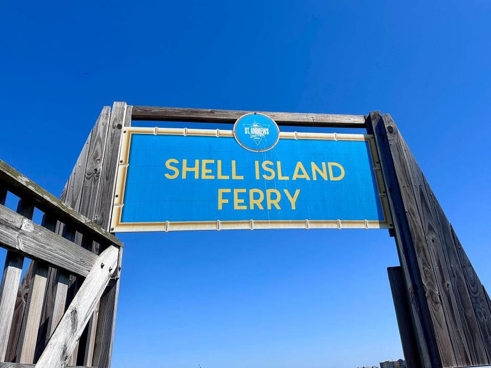 A blue sign with a yellow border supported by wooden beams at St. Andrews State Park entrance. The background is a bright-blue sky