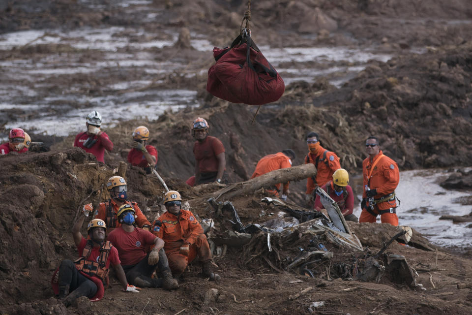 Firefighters watch the body of a person they pulled from the mud, as it is lifted up and taken away by a helicopter days after a dam collapse in Brumadinho, Brazil, Monday, Jan. 28, 2019. Firefighters on Monday carefully moved over treacherous mud, sometimes walking, sometimes crawling, in search of survivors or bodies four days after a dam collapse that buried mine buildings and surrounding neighborhoods with iron ore waste. (AP Photo/Leo Correa)