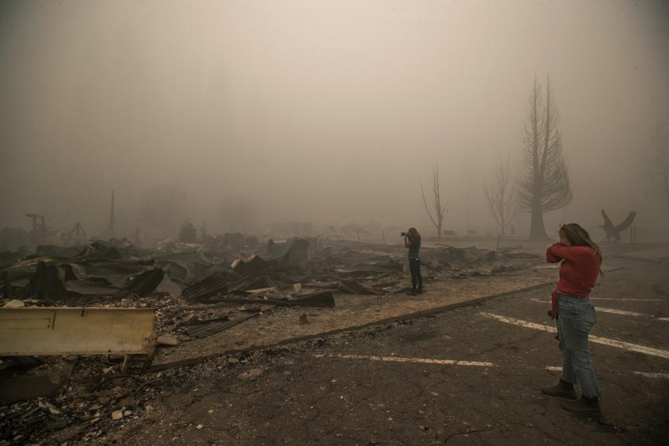 Tiffany Lozano, 44, right, covers her face from the smoke as her sister, Kelly Tan, 59, photographs what is left