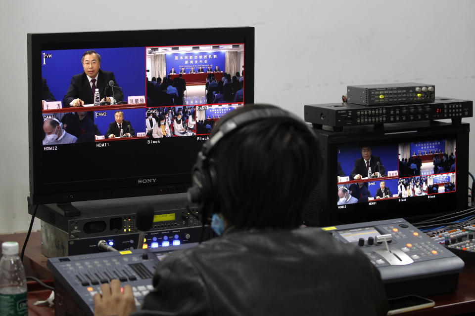 A worker watches Liu Jingzhen, chairman of the SinoPharm Group, speaks during a news conference of the Joint Prevention and Control Mechanism of the State Council at the National Health Commission in Beijing, Tuesday, Oct. 20, 2020. The state-owned Chinese drugmaker is setting up production lines to supply 1 billion doses of two possible coronavirus vaccines that are being tested on 50,000 people in 10 countries, Liu said. (AP Photo/Andy Wong)