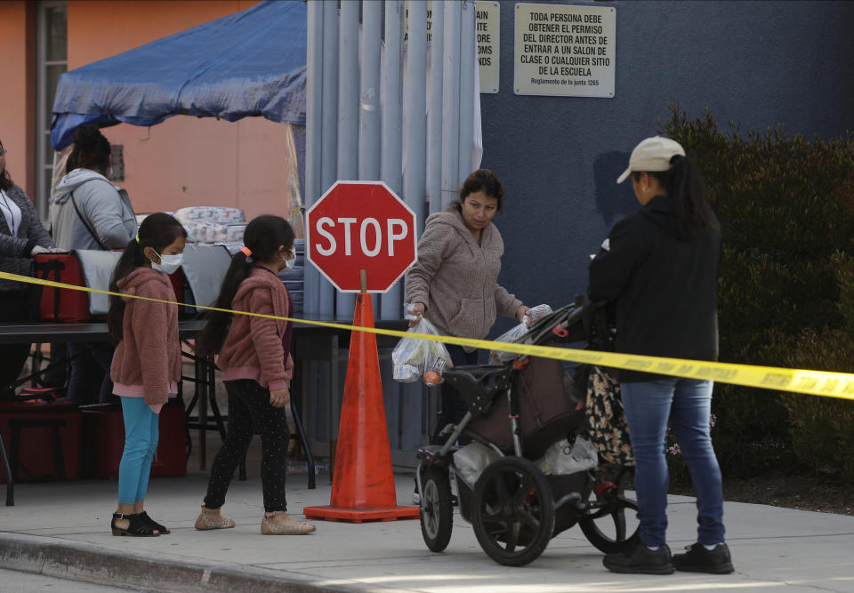 FILE - In this March 25, 2020, file photo, the Gomez family twin girls, with their mother from Oaxaca, Mexico, middle, pick up "Grab & Go" meals provided by the Los Angeles Unified District at the Robert F. Kennedy Community School station in Los Angeles. Amid spiking coronavirus cases, Los Angeles Unified School District campuses will remain closed when classes resume next month, Superintendent Austin Beutner said Monday, July 13, 2020, defying President Donald Trump's demand that students return to in-person instruction. (AP Photo/Damian Dovarganes, File)