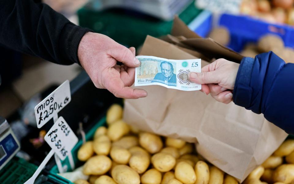 A customer (R) pays passes a stallholder a five pound note to pay for their fruit and vegetables at Walthamstow Market in east London on November 21, 2021. - TOLGA AKMEN/ AFP