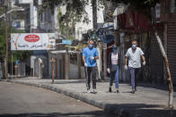 Palestinians wearing face masks walk next to closed shops in Gaza City, Thursday, Aug. 27, 2020. On Wednesday Gaza's Hamas rulers extended a full lockdown in the Palestinian enclave for three more days as coronavirus cases climbed after the detection this week of the first community transmissions of the virus in the densely populated, blockaded territory. (AP Photo/Khalil Hamra)