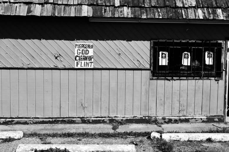 A sign attached to a deserted storefront says, “Please help, God. Clean-up Flint.”