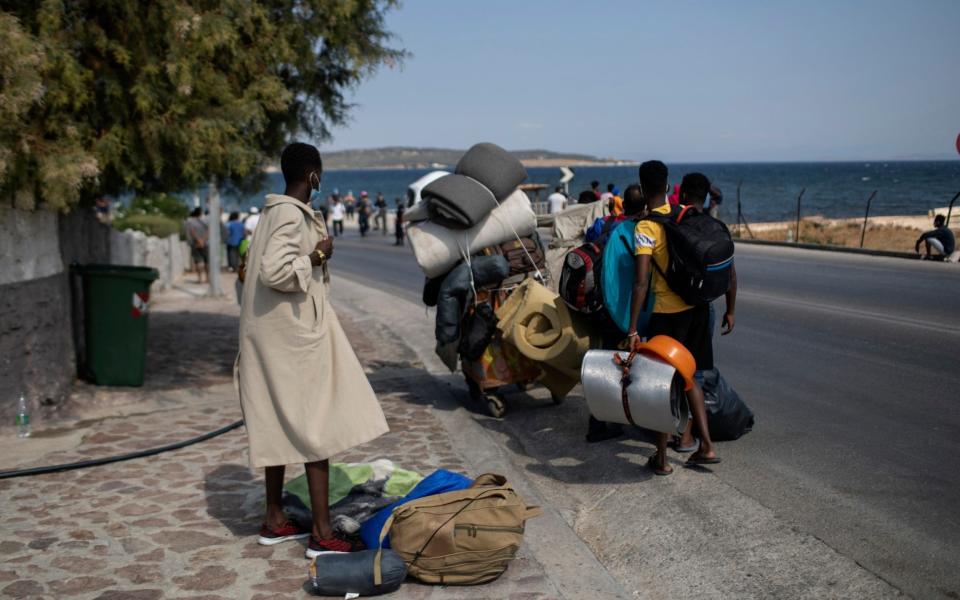 Migrants carrying their belongings, walk on a road near Mytilene town, on the northeastern island of Lesbos, Greece, - AP