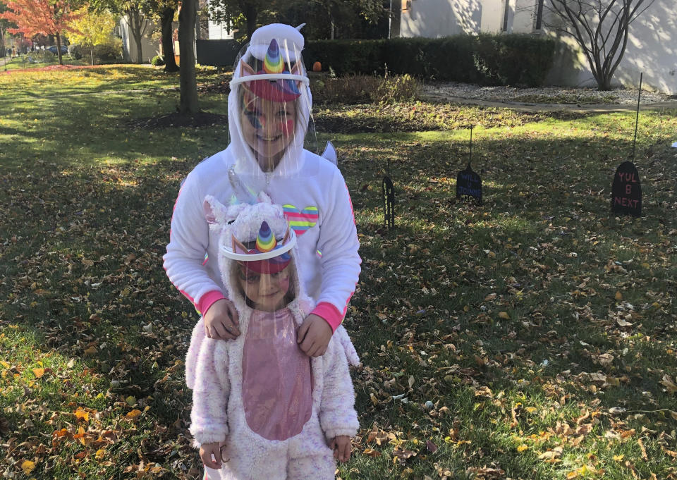 Ten-year-old Cameron Fox and her 4-year-old sister, Lexi, of Brookfield, Ill., are dressed as unicorns for Halloween with plastic face shields to protect against COVID-19, as they visit the home of family friends in nearby River Forest, Ill., on Saturday, Oct. 31, 2020. Their grandmother bought the shields as their mother, Julie, is taking them to visit the homes of friends and family in the area, in pace of the traditional trick-or-treating. (AP Photo/Don Babwin)