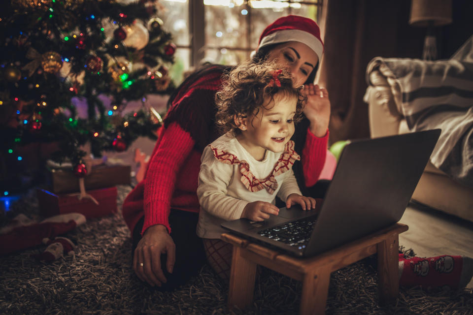 Mom and daughter have fun with cartoons on a laptop during Christmas. Christmas tree in the background