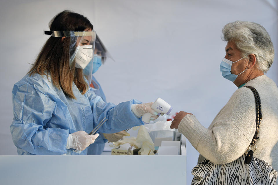 An electoral staff member checks the temperature of a woman, wearing a face mask for protection against the COVID-19 infection, before allowing her in a voting station in Bucharest, Romania, Sunday, Sept. 27, 2020. Some 19 million registered voters are choosing local officials, council presidents and mayors to fill more than 43,000 positions across the European Union nation. ( AP Photo/Vadim Ghirda)