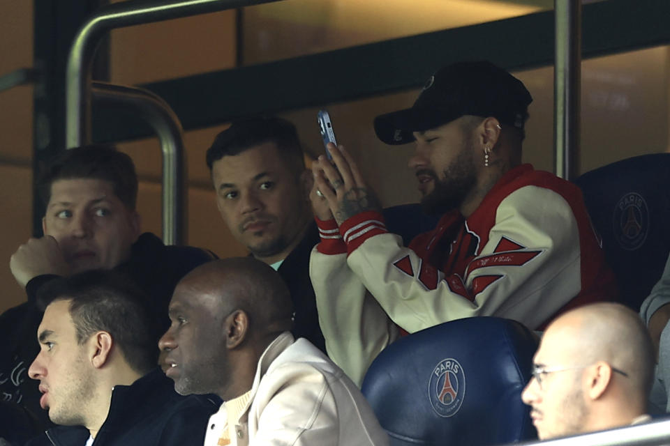 PSG's Neymar, right, uses his phone as he sits in the stands during the French League One soccer match between Paris Saint-Germain and Lorient, at the Parc des Princes stadium in Paris, Sunday, April 30, 2023. (AP Photo/Aurelien Morissard)