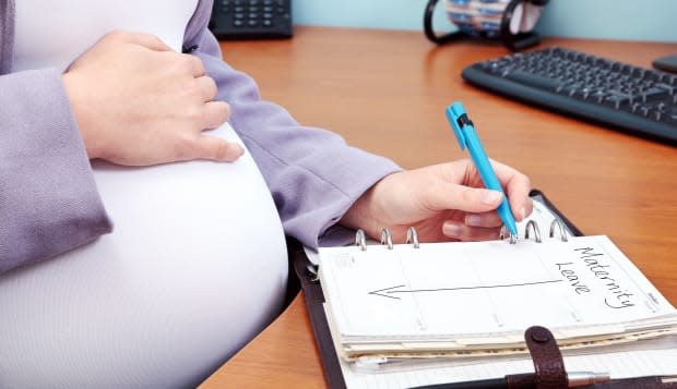 Photo of a pregnant woman in an office writing the words Maternity Leave in her diary.