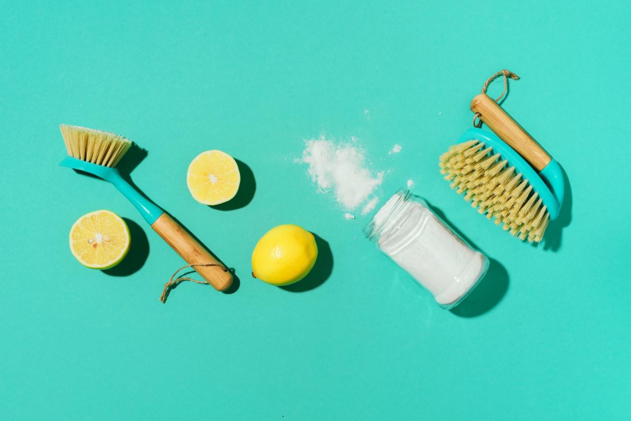 Baking soda, lemon, mustard powder and bamboo brushes against household chemicals products over blue background. Top view. Copy space. Flat lay. Effective and safe house cleaning.