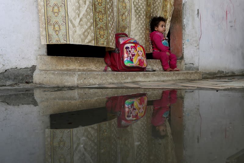 A girl is reflected in rainwater at the house of Palestinian man Eyad Al-Zahar in Gaza City