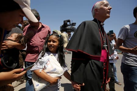 El Paso Bishop Mark Seitz walks along Honduran migrant Cesia and her parents at Paso del Norte international border crossing bridge to help them to ask for asylum in El Paso, Texas, U.S. as seen from Ciudad Juarez