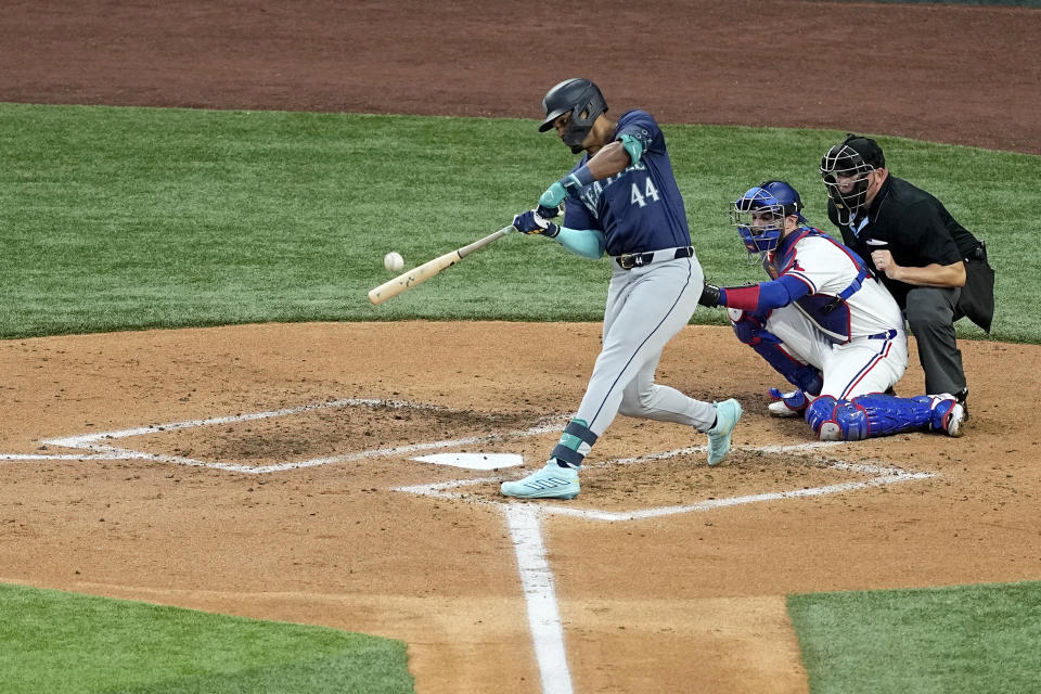 Seattle Mariners' Julio Rodriguez connects for a two-run home run next to Texas Rangers catcher Jonah Heim and umpire Mark Carlson during the third inning of a baseball game in Arlington, Texas, Tuesday, April 23, 2024. (AP Photo/Tony Gutierrez)