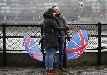 Tourists lower their Union Flag umbrellas as they take a selfie in the rain near Tower Bridge, in London, Britain January 15, 2017. REUTERS/Peter Nicholls/Files