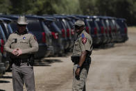 Texas Department of Public Safety officials stand near a lineup or vehicles parked near an encampment under the Del Rio International Bridge where migrants, many from Haiti, have been staying after crossing the Rio Grande, Thursday, Sept. 23, 2021, in Del Rio, Texas. The “amistad,” or friendship, that Del Rio, Texas, and Ciudad Acuña, Mexico, celebrate with a festival each year has been important in helping them deal with the challenges from a migrant camp that shut down the border bridge between the two communities for more than a week. Federal officials announced the border crossing would reopen to passenger traffic late Saturday afternoon and to cargo traffic on Monday. (AP Photo/Julio Cortez)