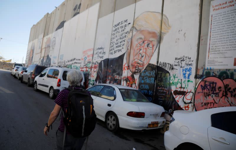 A tourist walks past a mural on the Israeli wall depicting U.S. President Donald Trump, in Bethlehem the Israeli-occupied West Bank