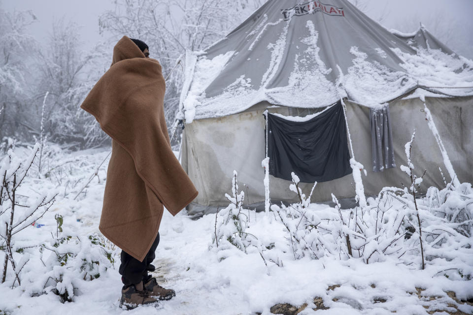 A migrant stands next to a snow covered tent at the Vucjak refugee camp outside Bihac, northwestern Bosnia, Tuesday, Dec. 3, 2019. A European human rights official has demanded immediate closure of a migrant camp in Bosnia where hundreds of people have started refusing food and water to protest dismal living conditions as wintry weather sets in. (AP Photo/Darko Bandic)