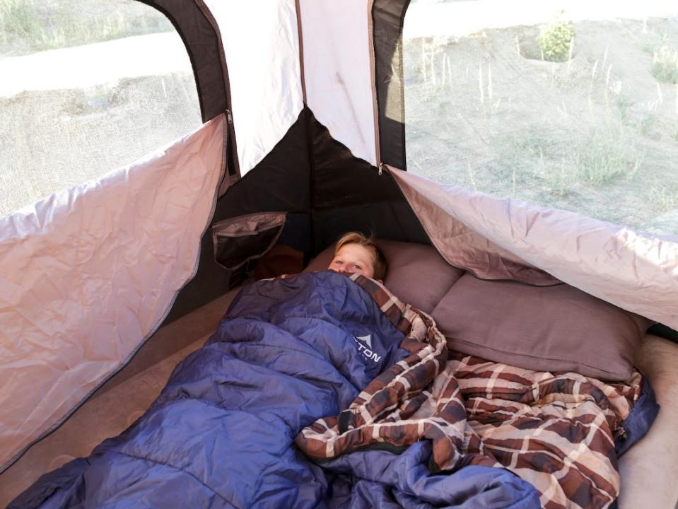 A child sleeping in a two-person sleeping bag in a tent while camping.